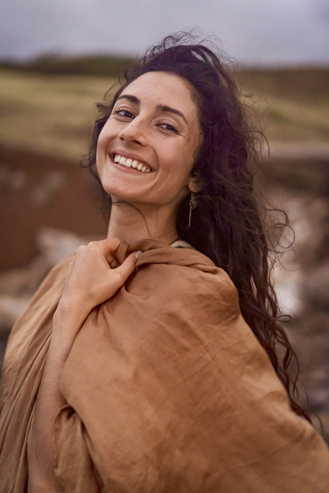 Mia smiling outdoors wrapped in warm earth-toned cloth