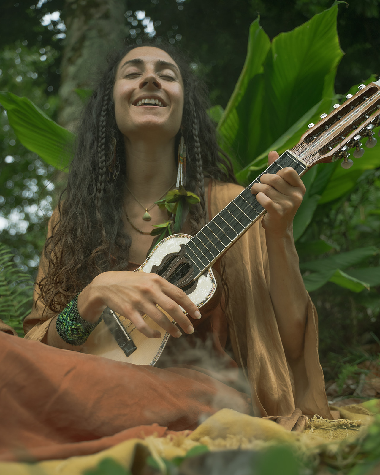 Mia smiling and playing a charango among lush green leaves